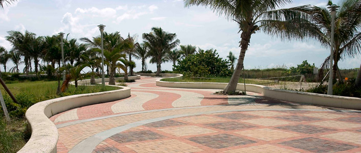 A photo of a wide concrete block paved curvy boulevard with two palm trees to the right hand side of the frame and several more to the left hand side background.